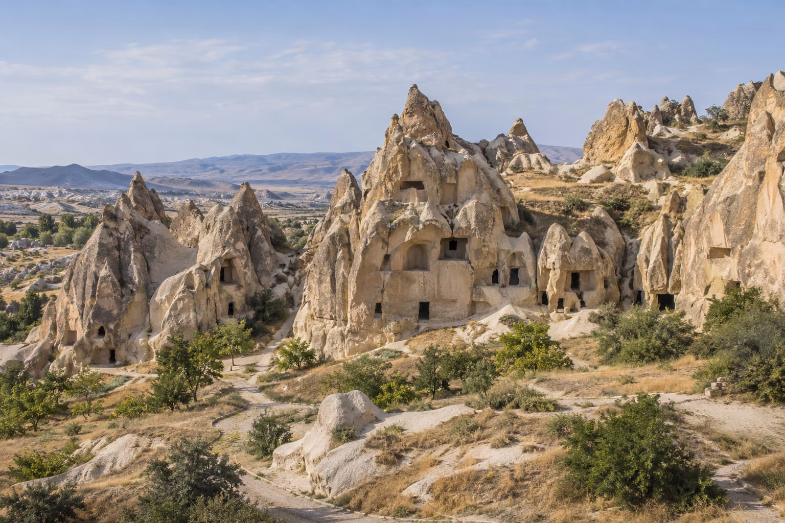 Recreación editorial diurna del paisaje rupestre de Göreme, con formaciones de toba y entradas talladas en la roca.
