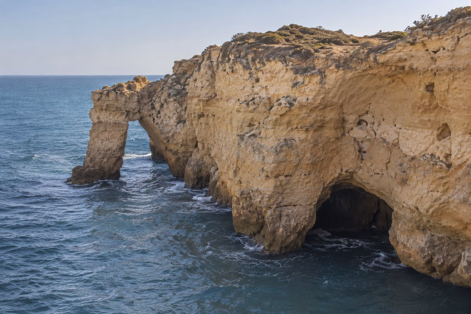 Recreación editorial de acantilado calcáreo con un arco y una cueva marina en el Algarve; no es una imagen documental exacta de Algar Seco.