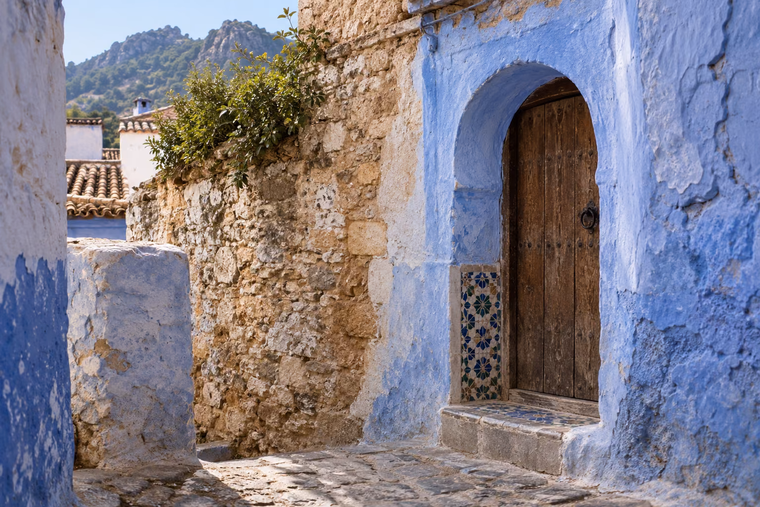 Recreación fotográfica editorial de un arco con puerta de madera, muro de piedra y cal y pared azul inspirada en la arquitectura de Chefchaouen.