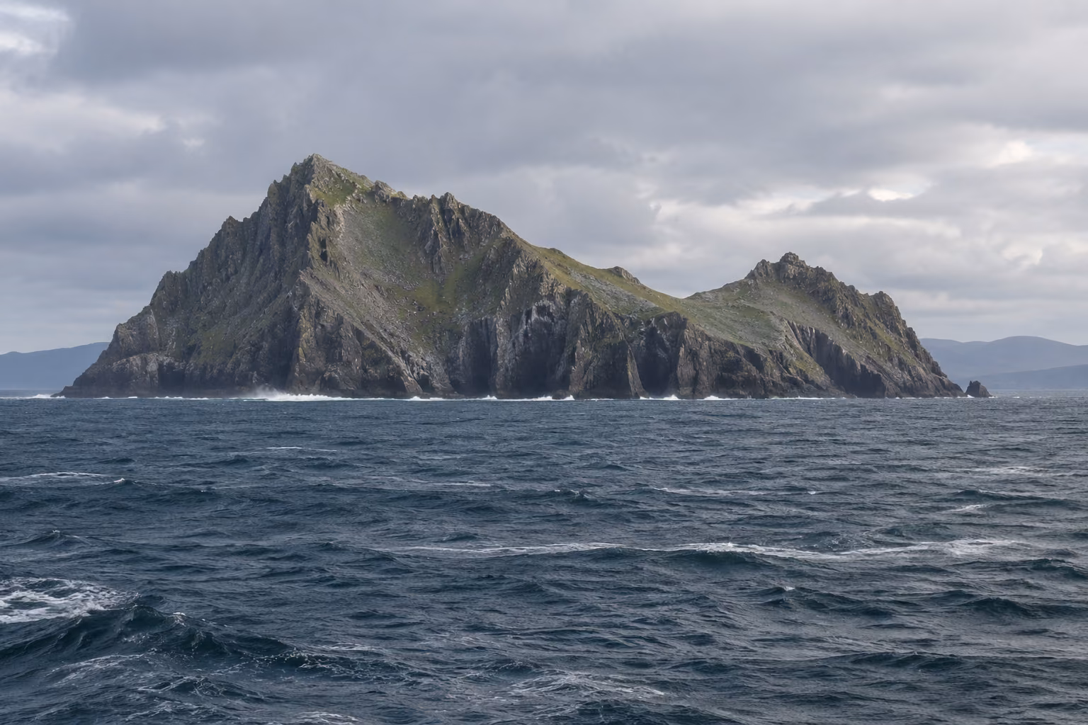 Recreación editorial de un islote atlántico con acantilados y laderas verdes, visto a distancia; no representa un avistamiento ni un día concreto en Skellig.